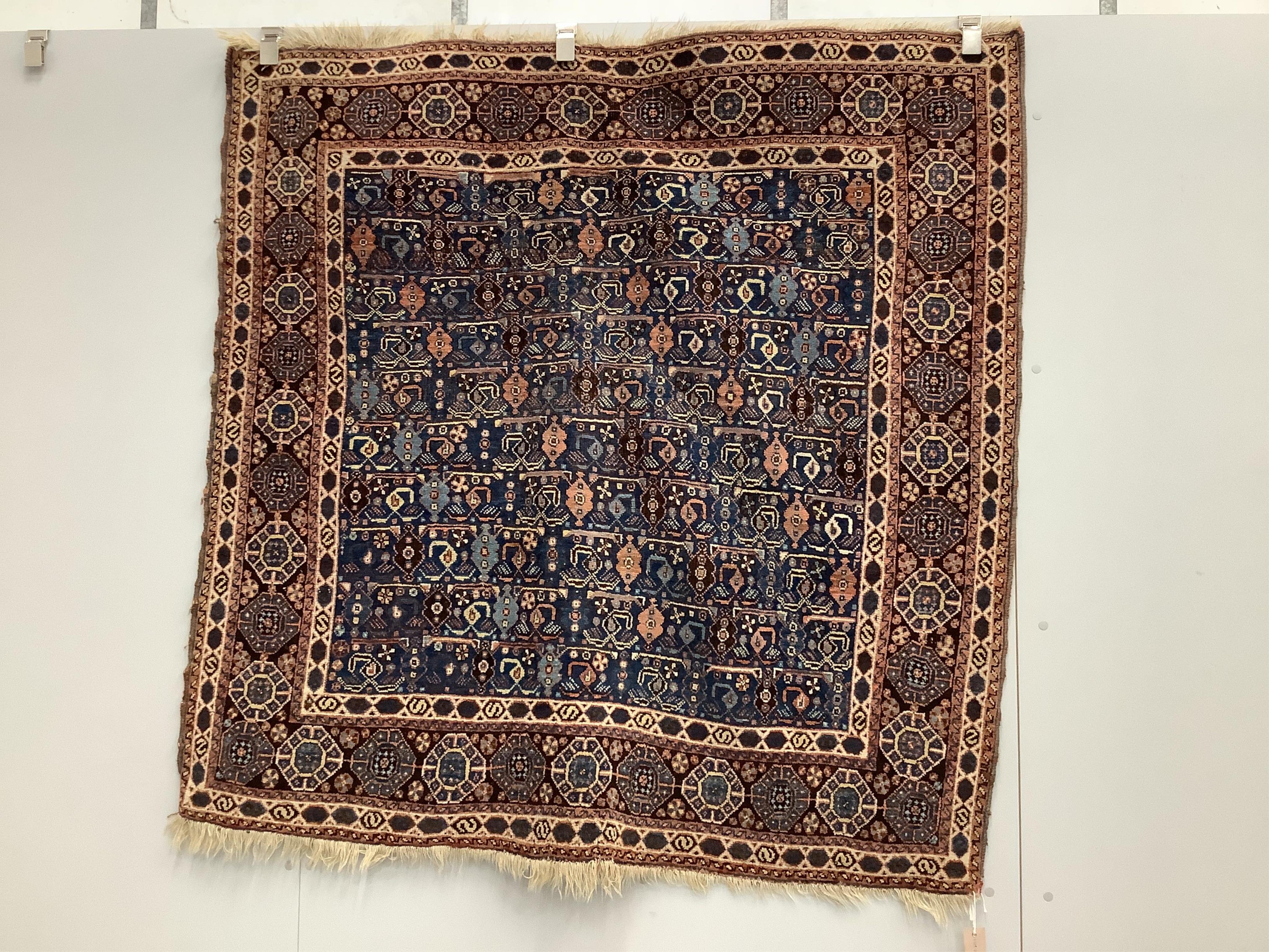 A Caucasian square shaped rug, woven with rows of hooked devices and shaped lozenges, on a blue field, 142 x 144cm